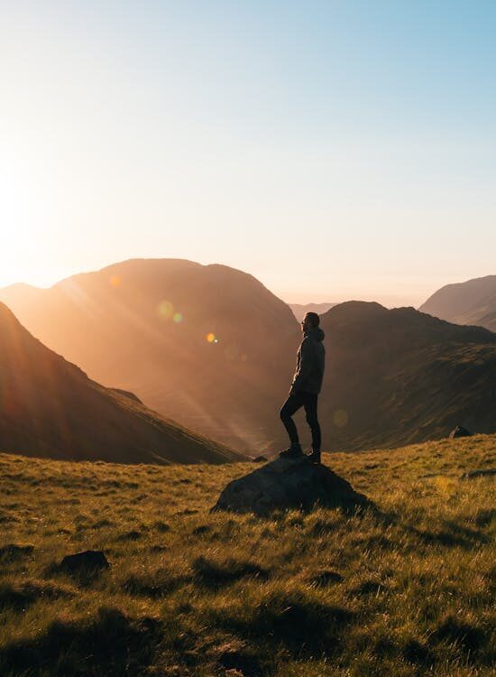 Silhouette of a person standing on a hill during sunrise in Cumbria, England with scenic mountain views.